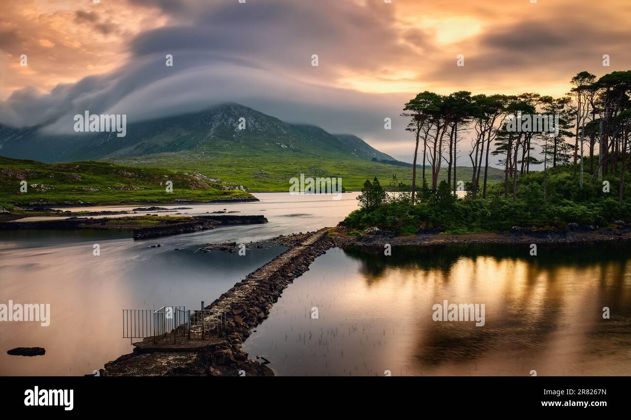 Wunderschöne Landschaft am Seeufer bei Sonnenaufgang mit zwölf Pinien im Wasser, umgeben von Bergen in Derryclare, connemara National Park in County Galway, Irland Stockfoto