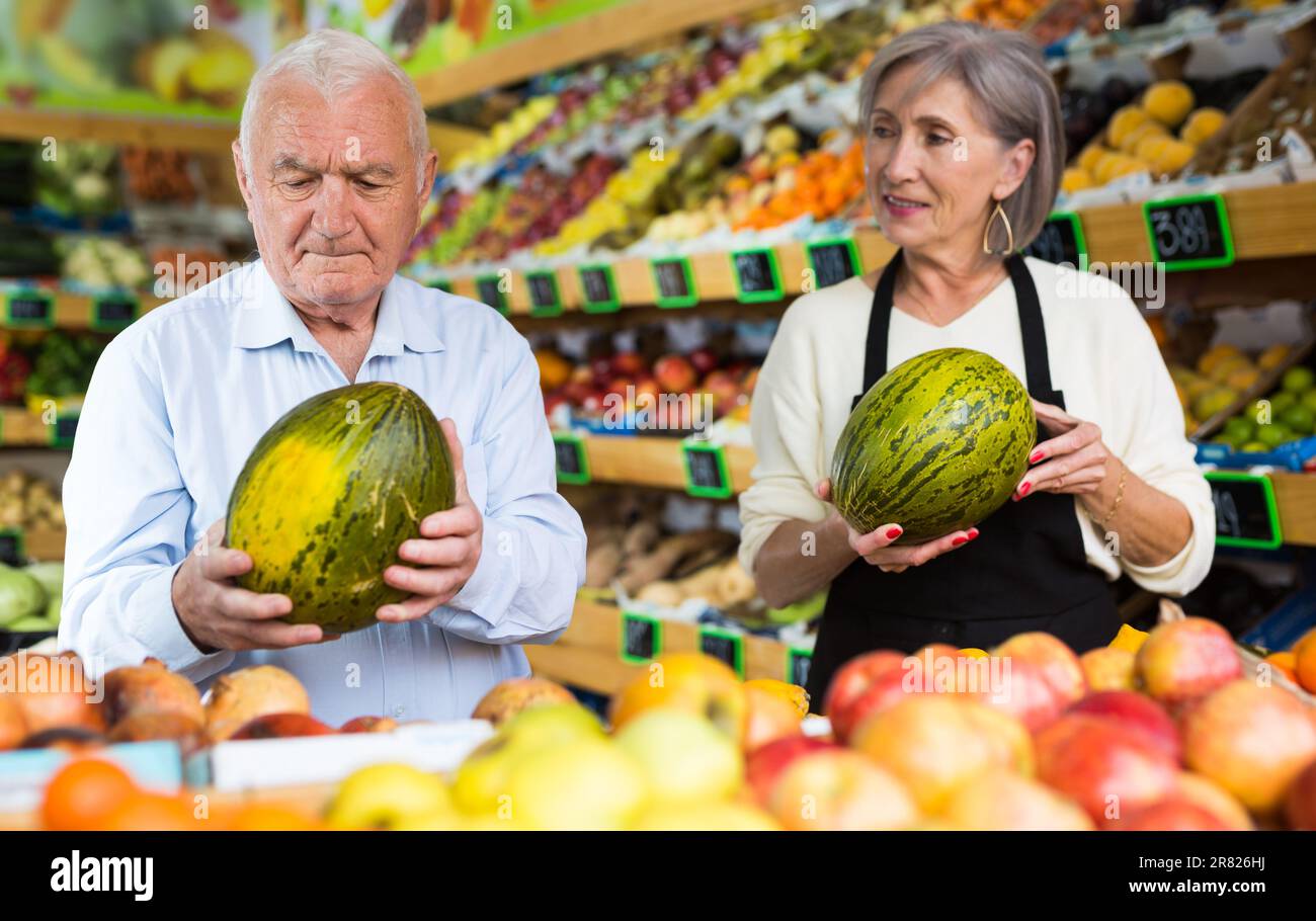 Dame im Gemüsehändler hilft dem alten Mann, Melone zu wählen Stockfoto