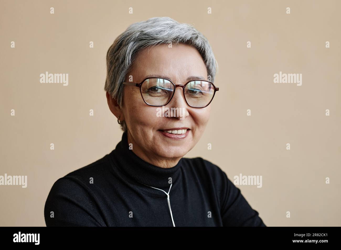 Hüftbild einer modernen asiatischen Seniorin, die in die Kamera schaut und eine Brille trägt Stockfoto