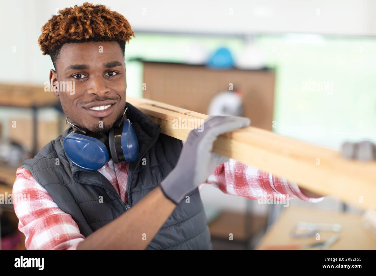 Junger Mann in Handschuhen mit Holzbrettern auf der Schulter Stockfoto