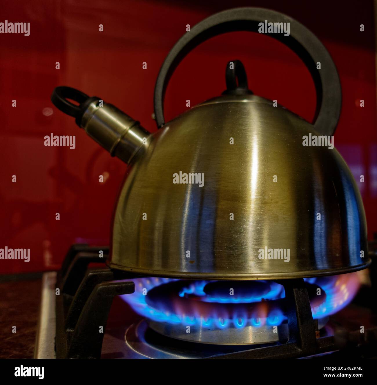 Ein Wasserkocher, der Wasser auf einem Treibgaskochfeld kocht. Blaue Flammen, die an der Seite des Wasserkochers lecken. Stockfoto