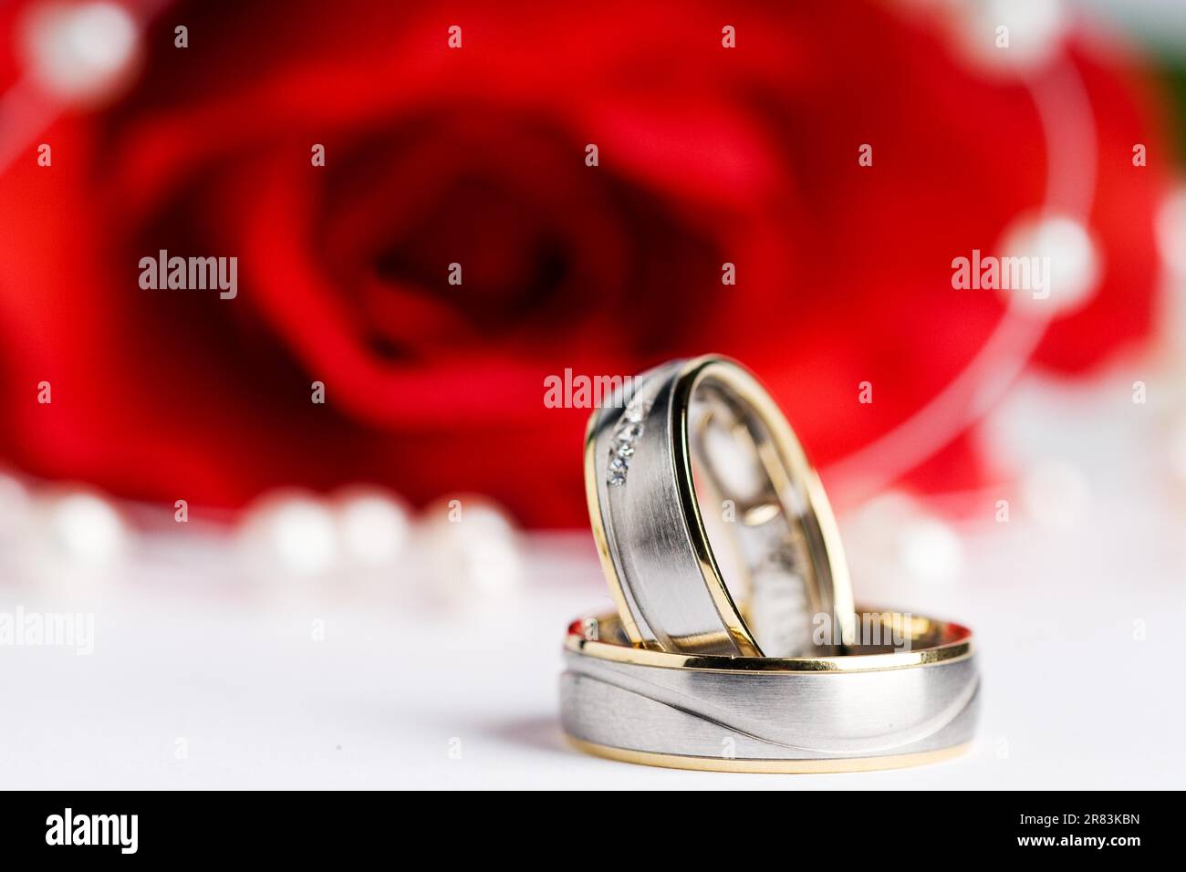 Zwei Ringe vor einer roten Rose und eine Perlenkette Stockfoto