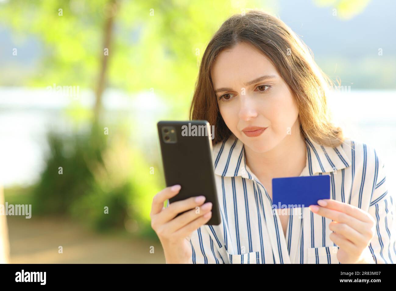 Enttäuschter Online-Käufer, der sein Telefon überprüft und seine Kreditkarte in der Natur hält Stockfoto