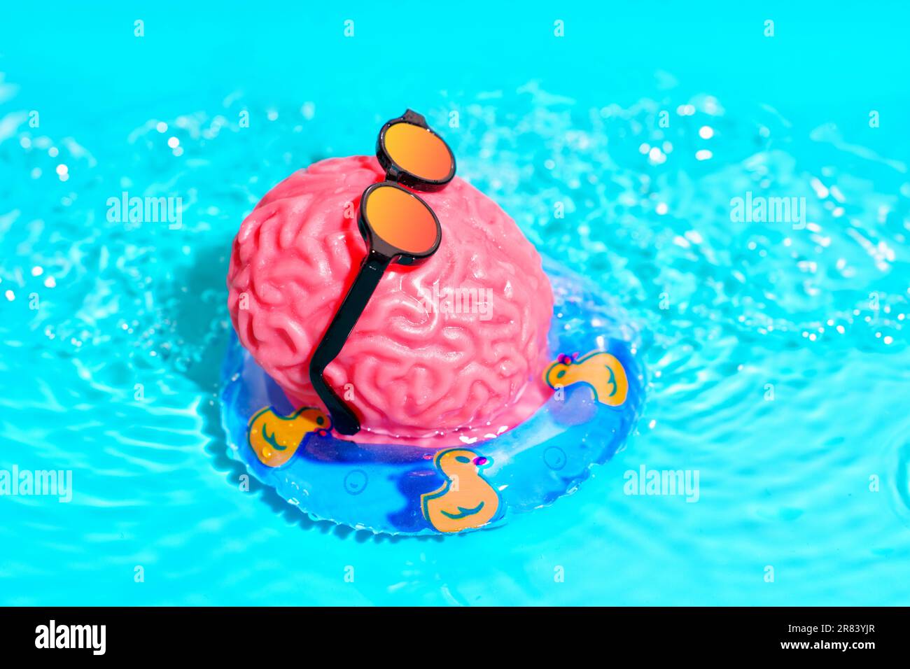 Die pinkfarbene Figur des menschlichen Gehirns trägt eine trendige Sonnenbrille und schwimmt mühelos in einem Pool auf einer aufblasbaren Röhre mit süßen Enten. Geistige Rejuvenatio Stockfoto