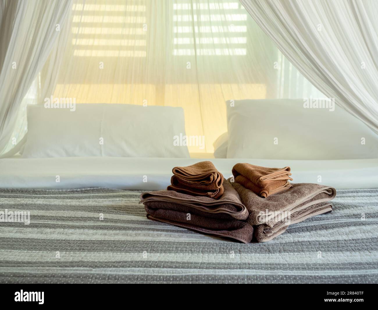 Set brauner Handtuchfalten, dekoriert auf Matratzenbett mit gestreifter Decke und weißem Moskitonetz in der Nähe des Holzfensters im Hotelzimmer, asiatische Stockfoto