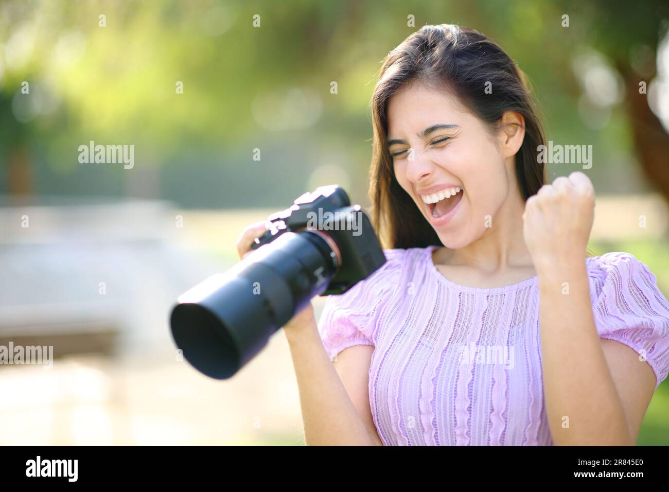 Aufgeregter Fotograf in einem Park, der die Ergebnisse mit einer spiegellosen Kamera überprüft Stockfoto