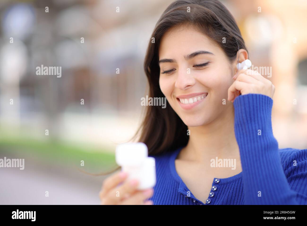 Glückliche Frau, die auf der Straße schnurlose Ohrstöpsel aufsetzt Stockfoto