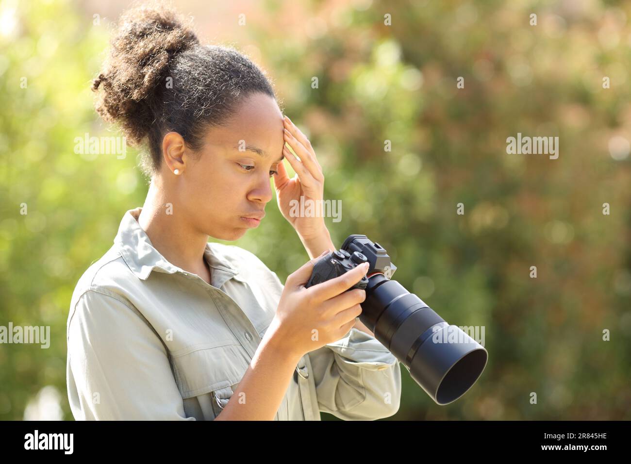 Besorgter schwarzer Fotograf, der die Kamerainhalte in einem Park überprüft Stockfoto