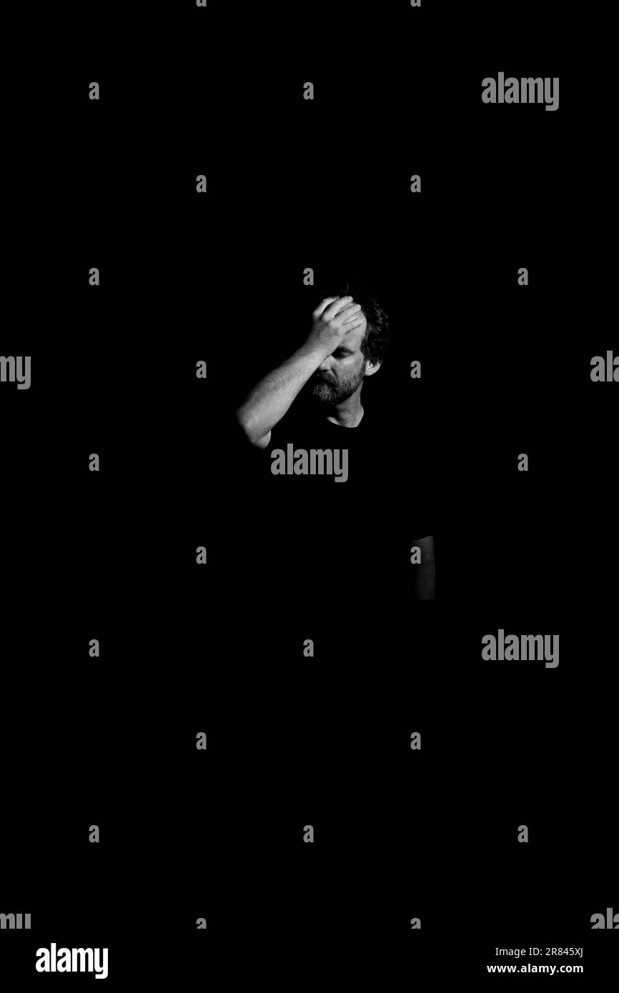 Ein weißer Mann, der seinen Kopf hielt, während er in einem dunklen Raum erstrahlte. Stockfoto