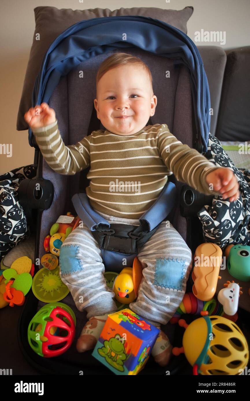 Porträt eines süßen Jungen im Kinderwagen, umgeben von bunten Spielzeugen. Liebe und Familiengefühle Stockfoto