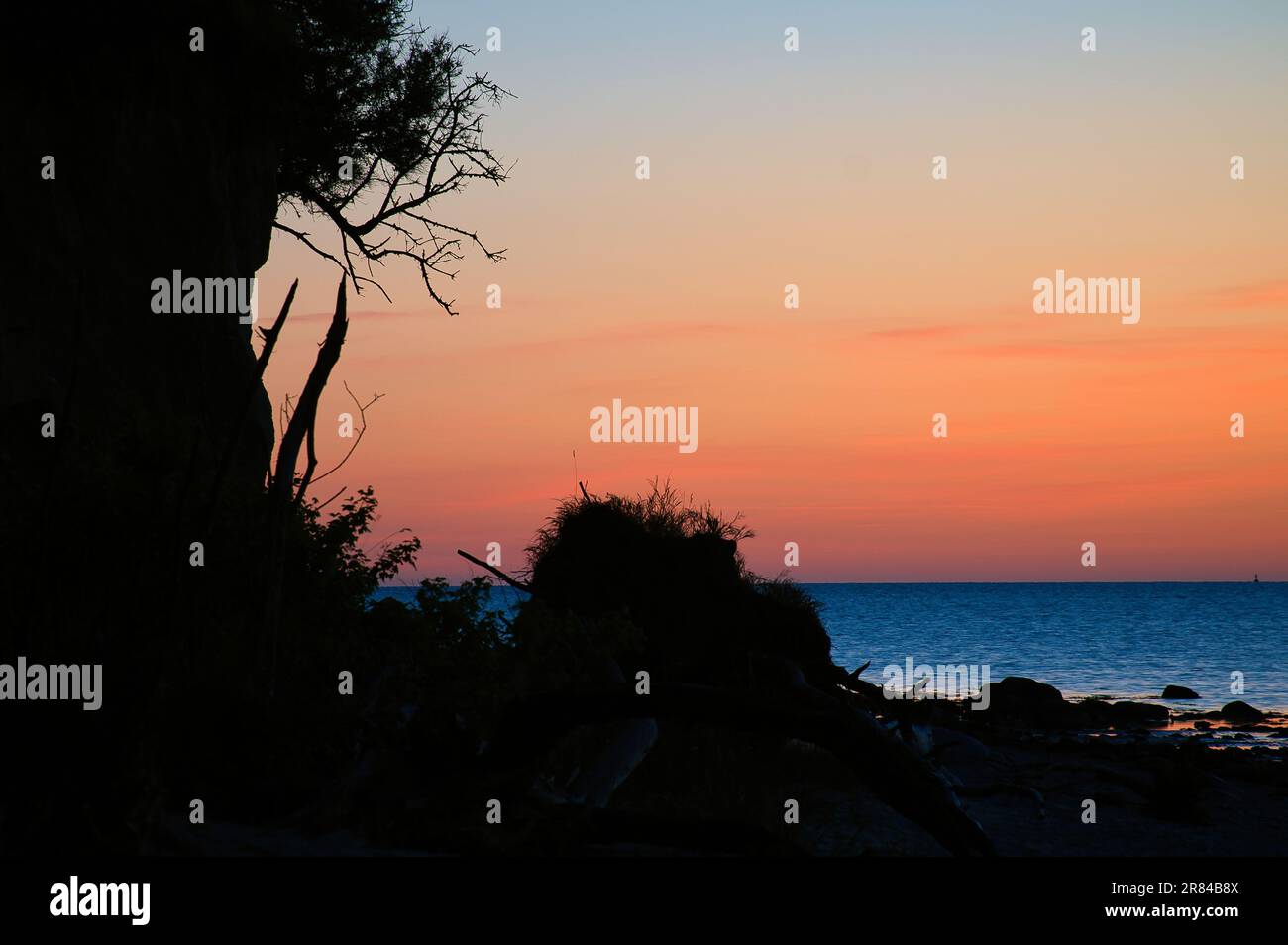Steile Küste auf der Insel Poel bei Sonnenuntergang mit Blick auf den pastellfarbenen Himmel über Felsen in der Ostsee. Landschaftsaufnahmen von der Küste Stockfoto