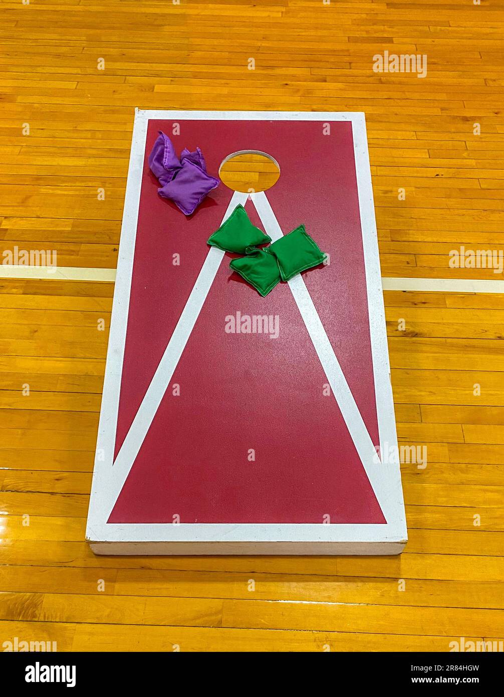 Corn-Hole-Spiel mit bunten Bohnenbeuteln auf dem Boden des Fitnessstudios, das für Gymnastikstunden in der Highschool verwendet wird. Stockfoto