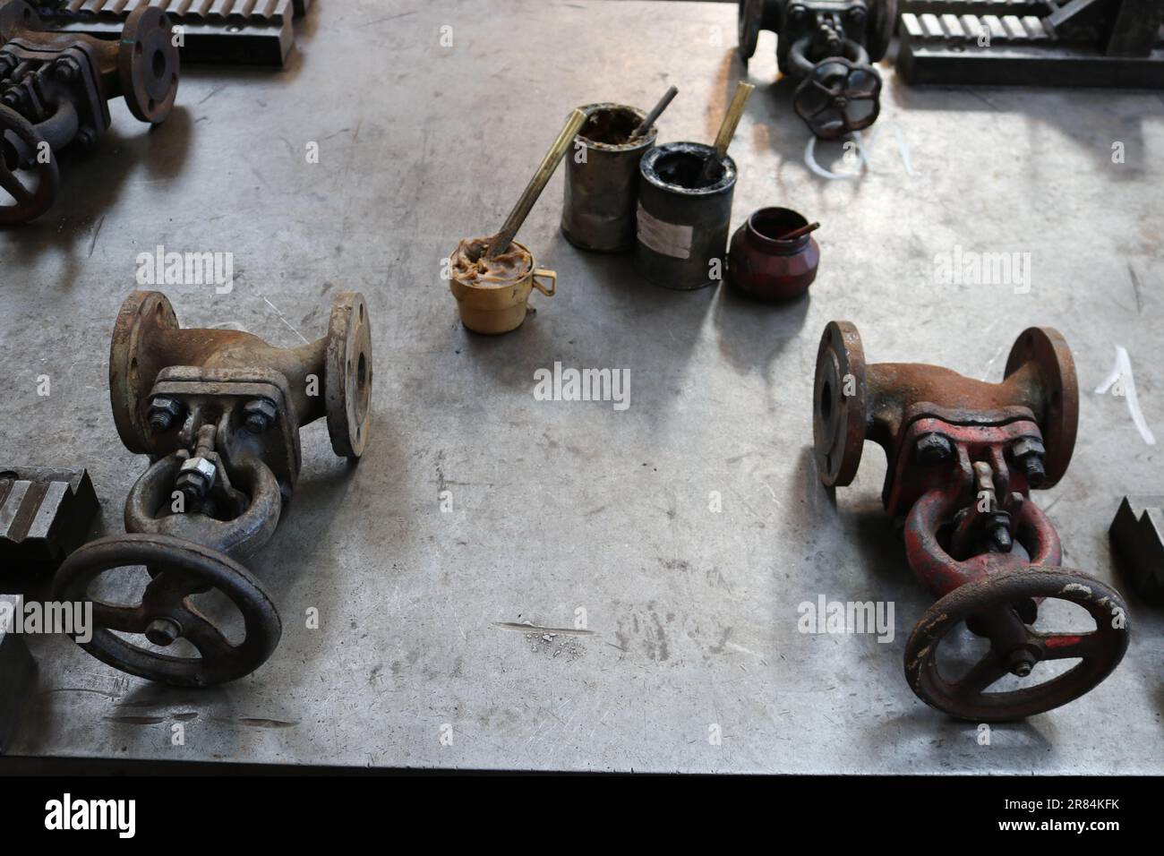 Zwei alte Metallschlösser, Rohrverbindungen, Dosen mit Graphitfett, Feststoff auf einem großen Eisentisch in der Fabrik, Werkstatt. Stockfoto