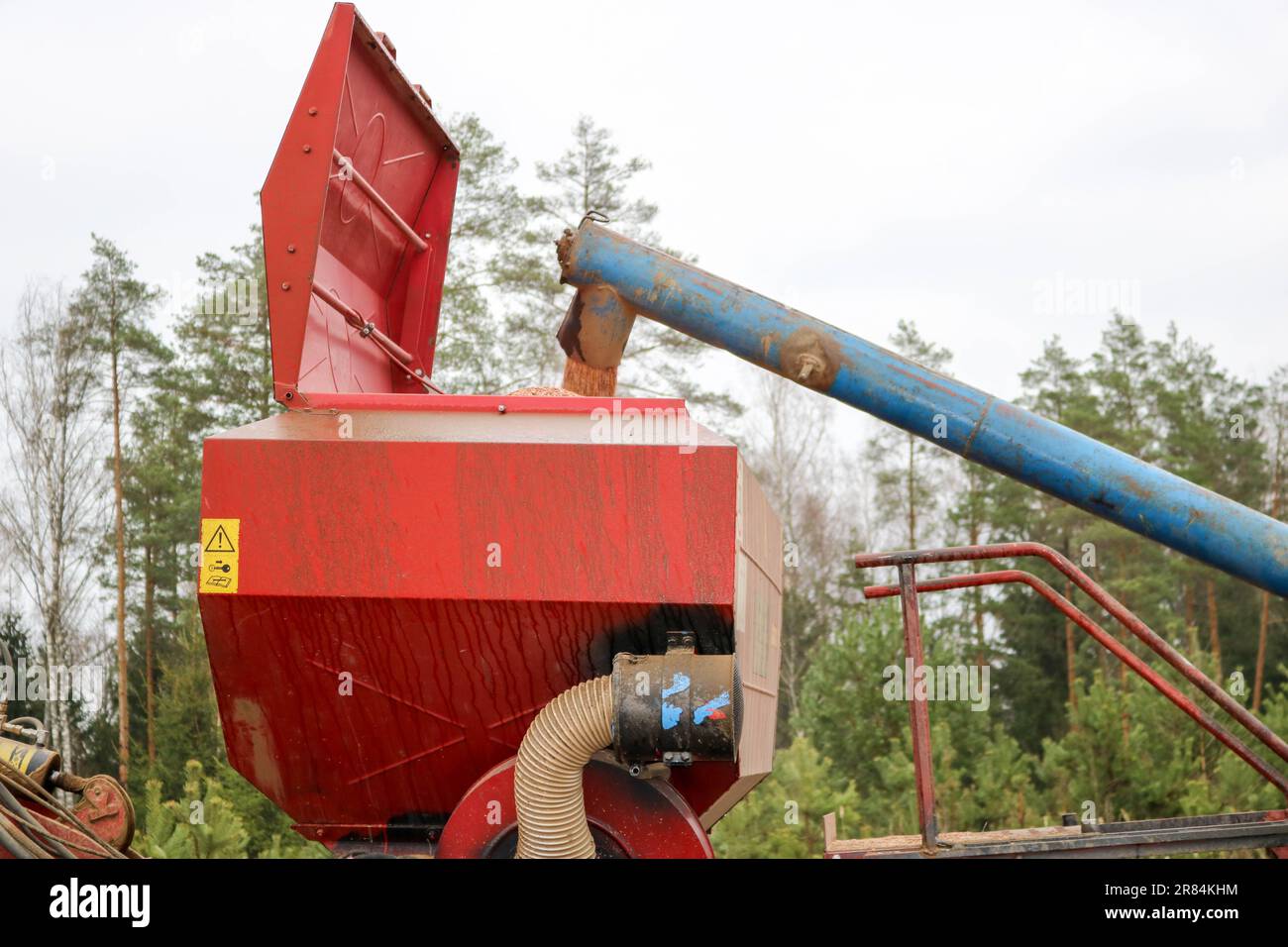 Das Korn aus dem Rohr fällt in eine große, rote Sägemaschine, einen Mähdrescher mit großen Rädern zum Pflügen des Bodens, eine Maschine zum Aussäen von Getreide, leistungsstark Stockfoto