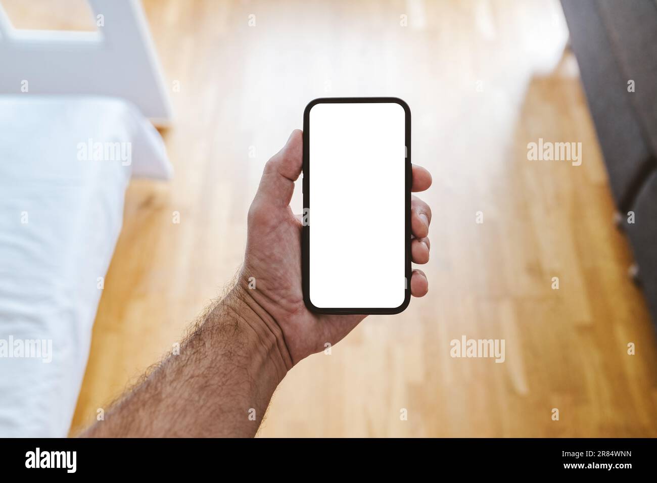 Mann mit Smartphone-Gerät und leerem Mockup-Bildschirm im Schlafzimmer. Speicherplatz für App oder Textnachricht kopieren. Selektiver Fokus. Stockfoto