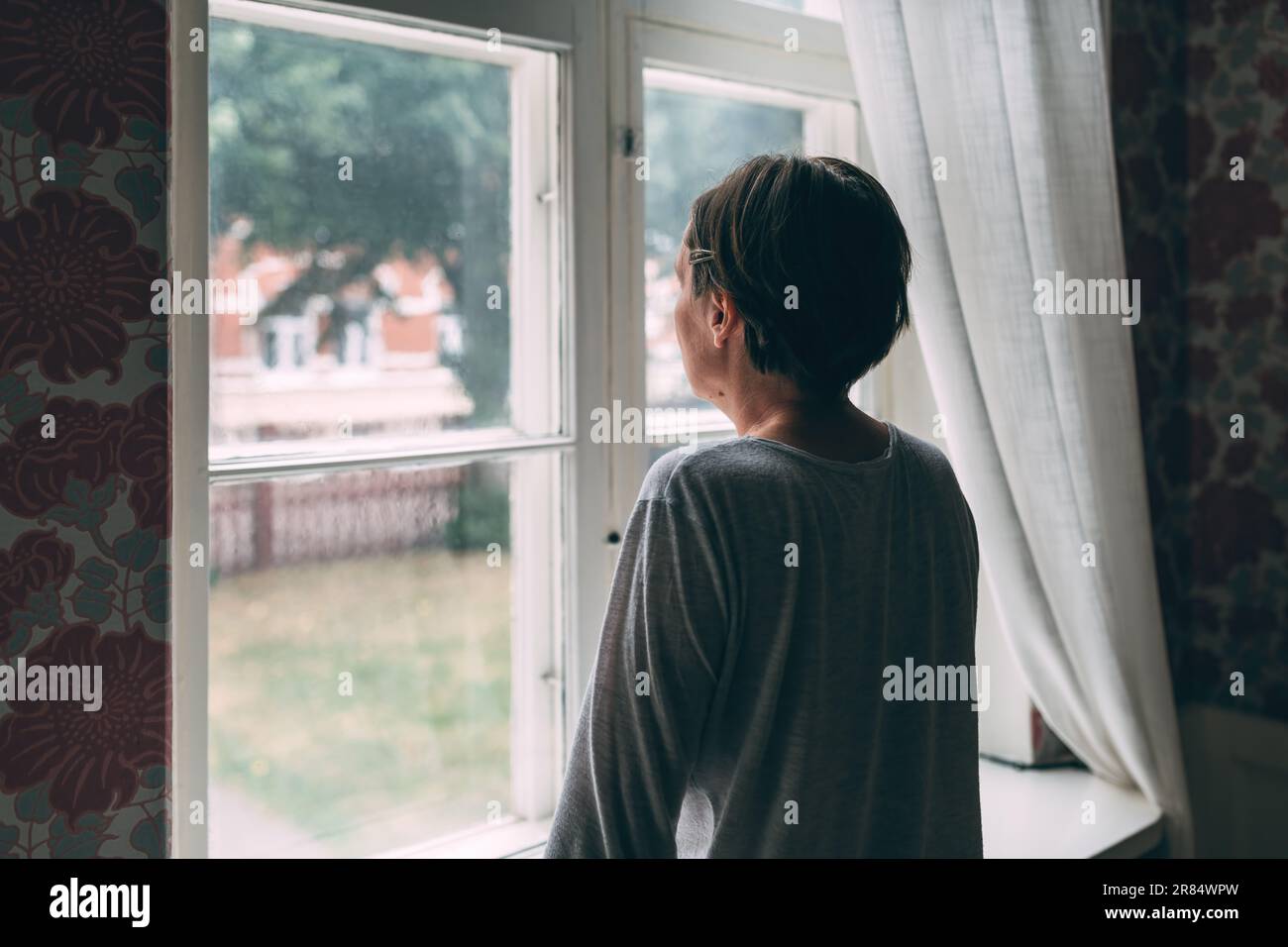 Introspektive mittelErwachsene Frau, die aus dem Fenster schaut und einen selektiven Fokus in Betracht zieht Stockfoto