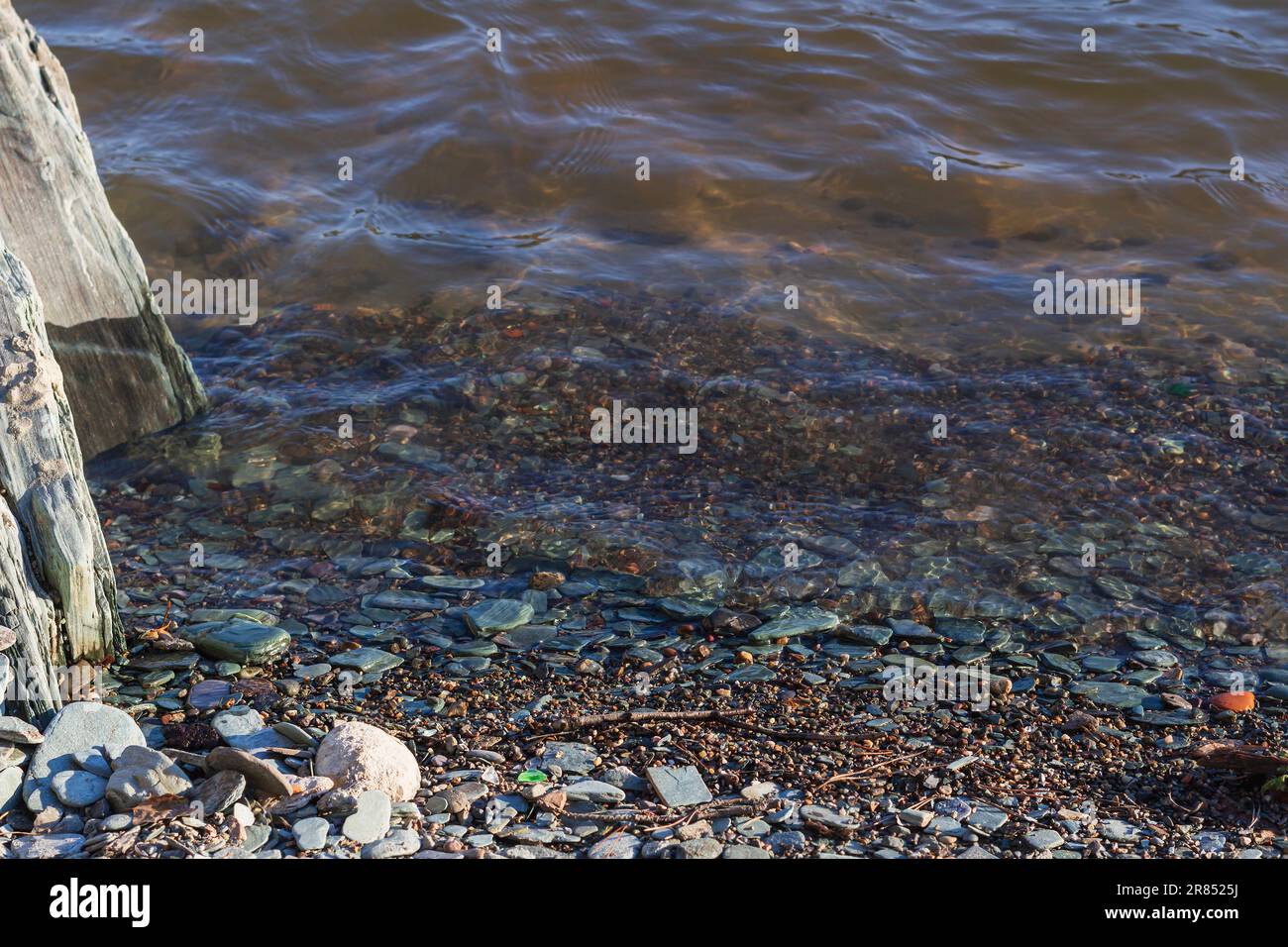 ufer des Bergflusses bei Sonnenuntergang, selektiver Fokus, Kopierraum. Ein bunter Plan. Kleine flache Steine, wie Pfannkuchen, schimmern mit Farben von den Gegenständen Stockfoto