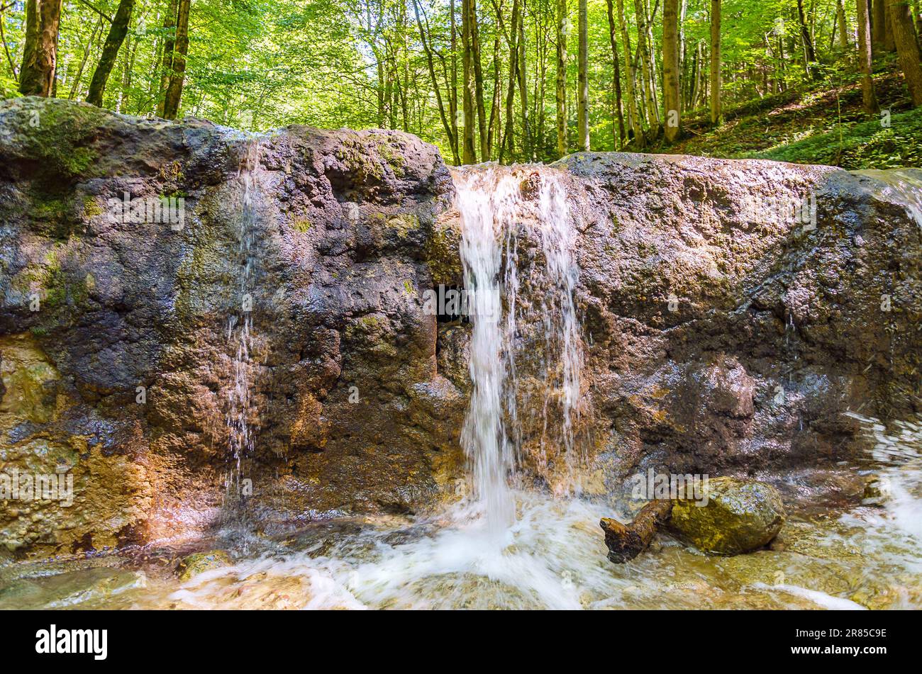 Kleiner Wasserfall eines Bachs an einem sonnigen Sommertag. Klares Wasser eines Bachs fließt über einen alten Damm, der als Torrent-Kontrolle gebaut wurde. Entspannende und friedliche Atmosphäre. Stockfoto