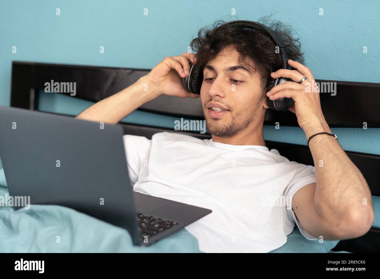 Ein junger arabischer Mann, der ein Notebook mit Kopfhörern benutzt und sich zu Hause im Bett einen Film ansieht. Werbung im Internet und Freiberufler im Bildungsbereich Stockfoto