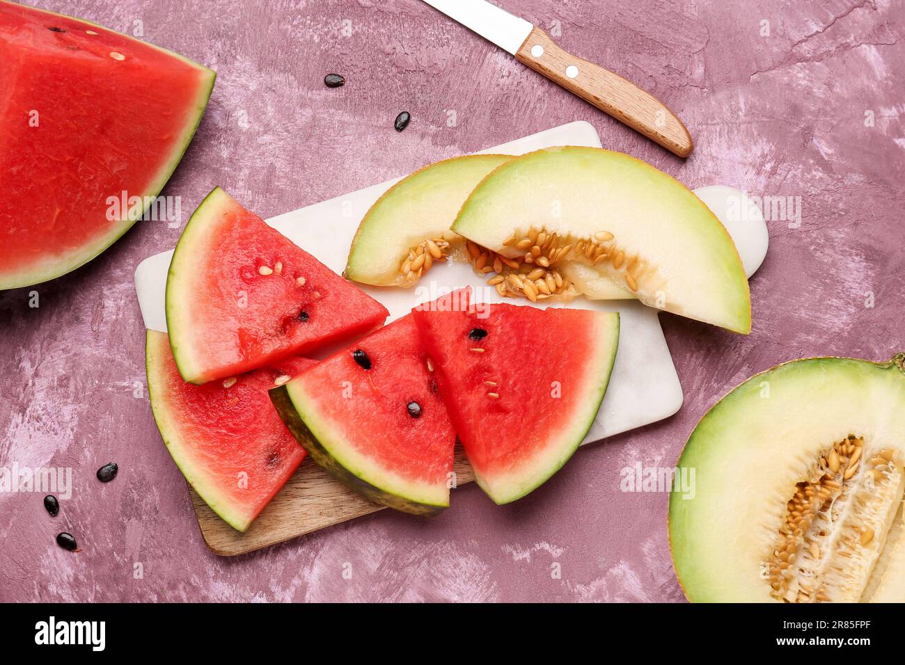 Brett mit frischen Wassermelonen und Melonen auf lila Hintergrund Stockfoto