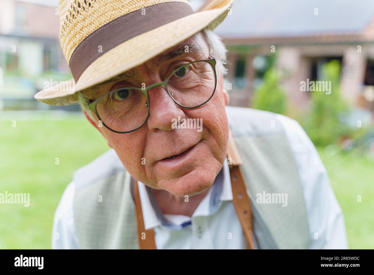 Ein fröhlicher und leicht betrunkener Senior Mann, der einen Strohhut, ein Hemd, eine Brille und eine Schürze trägt, sieht merkwürdigerweise in die Kamera. Das Foto wurde gemacht Stockfoto