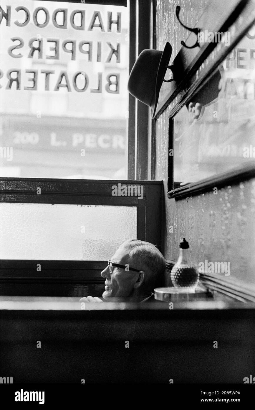 Charley's Dining Rooms in the City of London 1960er. Auf der Speisekarte - auf das Fenster gemalt sind Schellfisch, Kippers, Bloater. (Bloater sind eine Art kaltgeräucherter Hering.) Sie werden leicht geraucht, ohne auszunehmen, was einen charakteristischen, leicht geilen Geschmack verleiht. Wenn man darauf wartet, dass sein Mittagessen serviert wird, und an einem Tisch mit hoher Rückenlehne sitzt, hängt ein Mann seinen Trilby-Hut auf einen Stift über seinem Kopf. London, England, ca. 1969. HOMER SYKES AUS GROSSBRITANNIEN Stockfoto