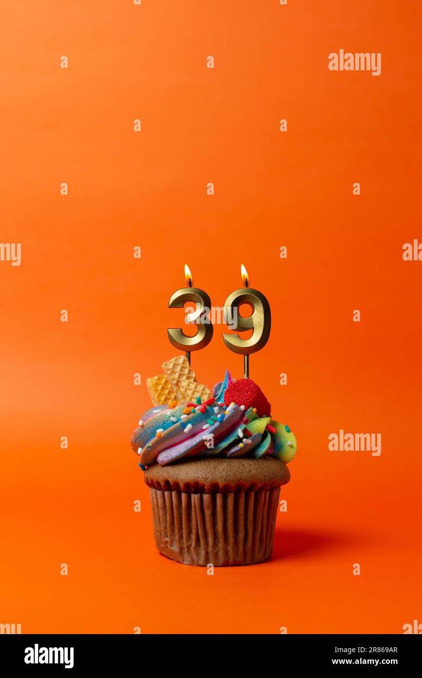 Geburtstagskuchen mit Nummer 39 - Cupcake auf orangefarbenem Hintergrund mit Geburtstagskerzen Stockfoto