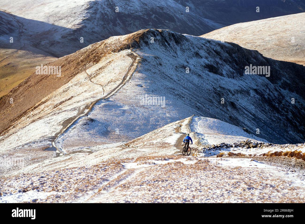 Ein Mountainbiker auf einem felsigen Pfad vom Gipfel des Grisedale Pike in Richtung Sand Hill und Hopegill Head im Winter im English Lake District Stockfoto