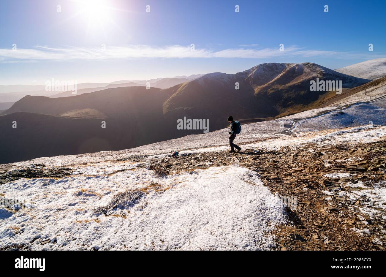 Eine Wanderer und ihr Hund laufen von Grisedale Pike nach Sand Hill mit Crag Hill in der Ferne im Winter im englischen Lake District, Großbritannien. Stockfoto