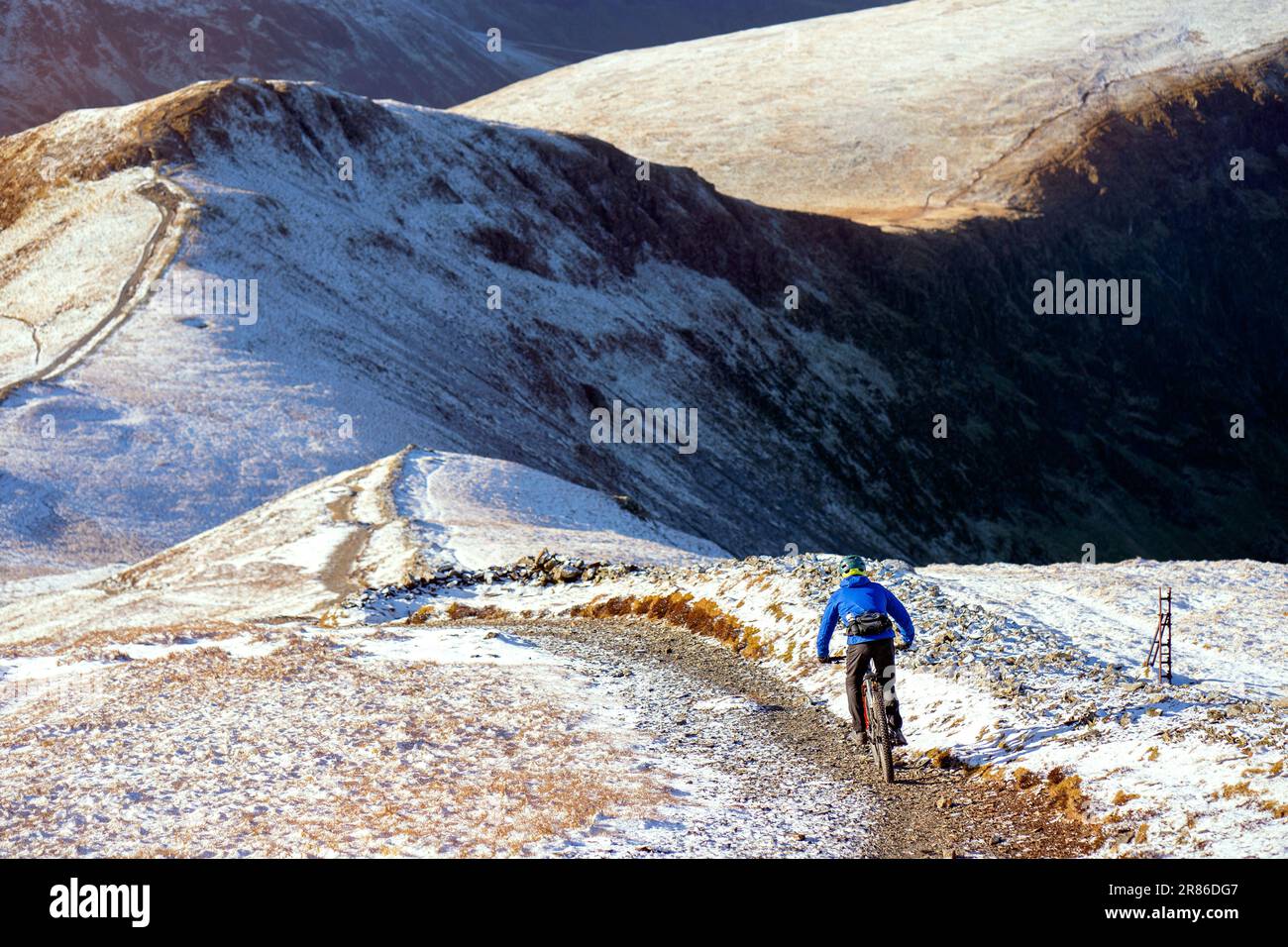Ein Mountainbiker auf einem felsigen Pfad vom Gipfel des Grisedale Pike in Richtung Sand Hill und Hopegill Head im Winter im English Lake District Stockfoto