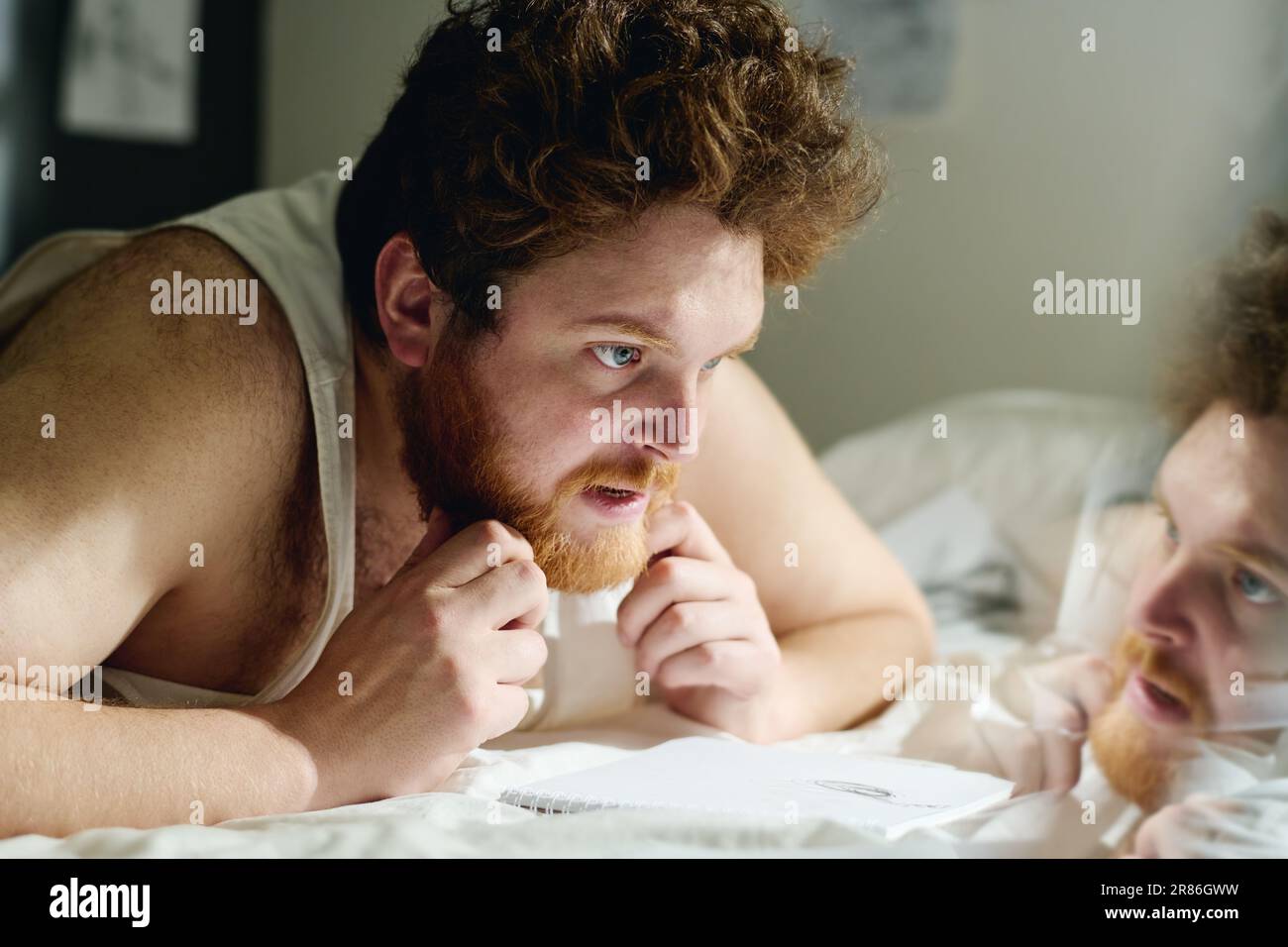 Junger pensiver Mann mit Angststörung, der sich auf Stationen der Nervenklinik über das Bett bückt und dabei an Ideen denkt, bevor er seine Phobien zeichnet Stockfoto