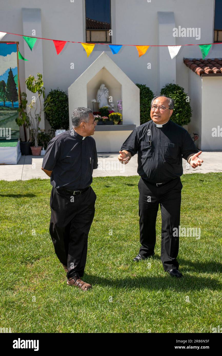 Hispanic und ein vietnamesischer amerikanischer Priester vor einem Schrein für die Heilige Mutter in einer katholischen Kirche in Südkalifornien. Stockfoto