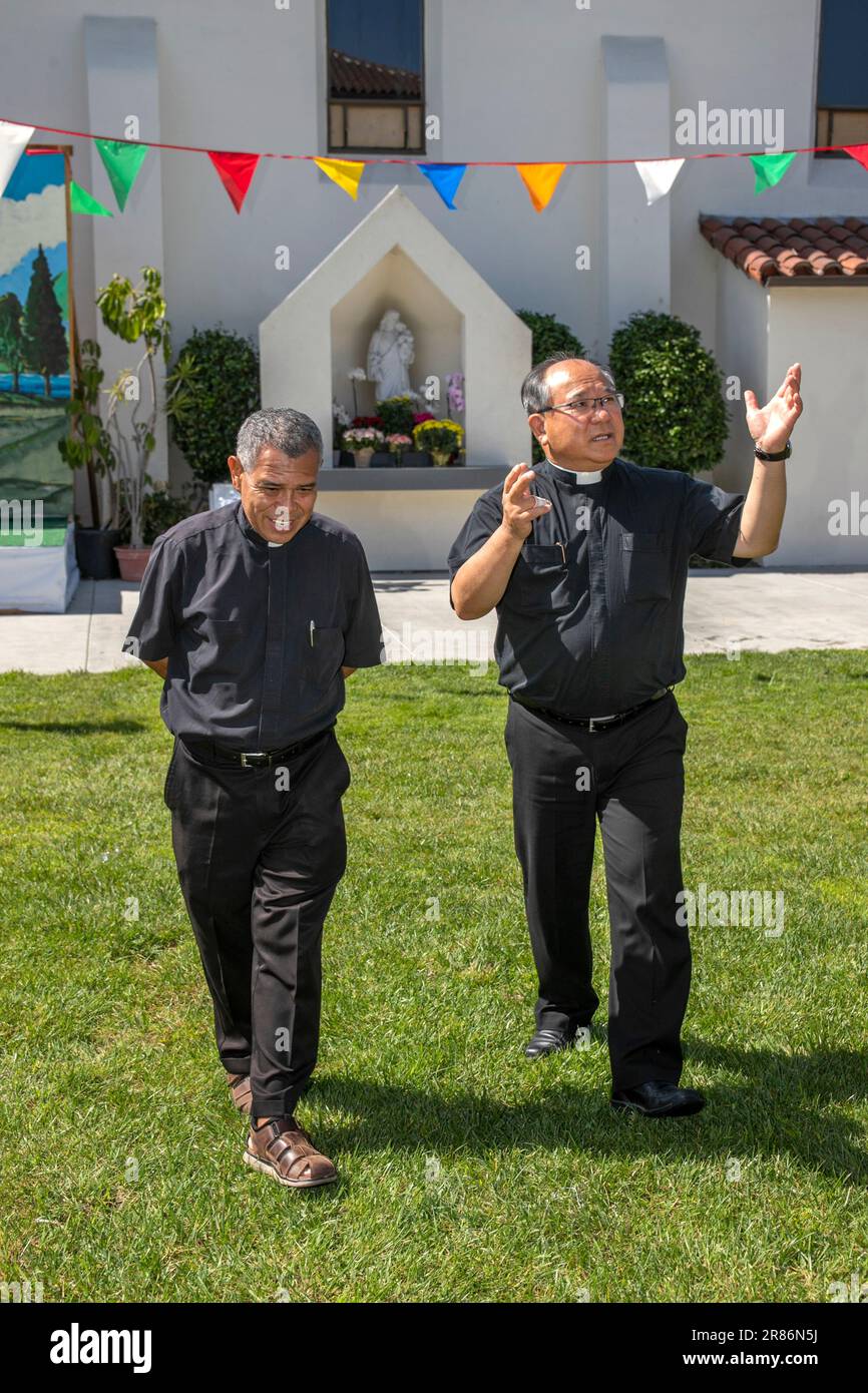 Hispanic und ein vietnamesischer amerikanischer Priester vor einem Schrein für die Heilige Mutter in einer katholischen Kirche in Südkalifornien. Stockfoto