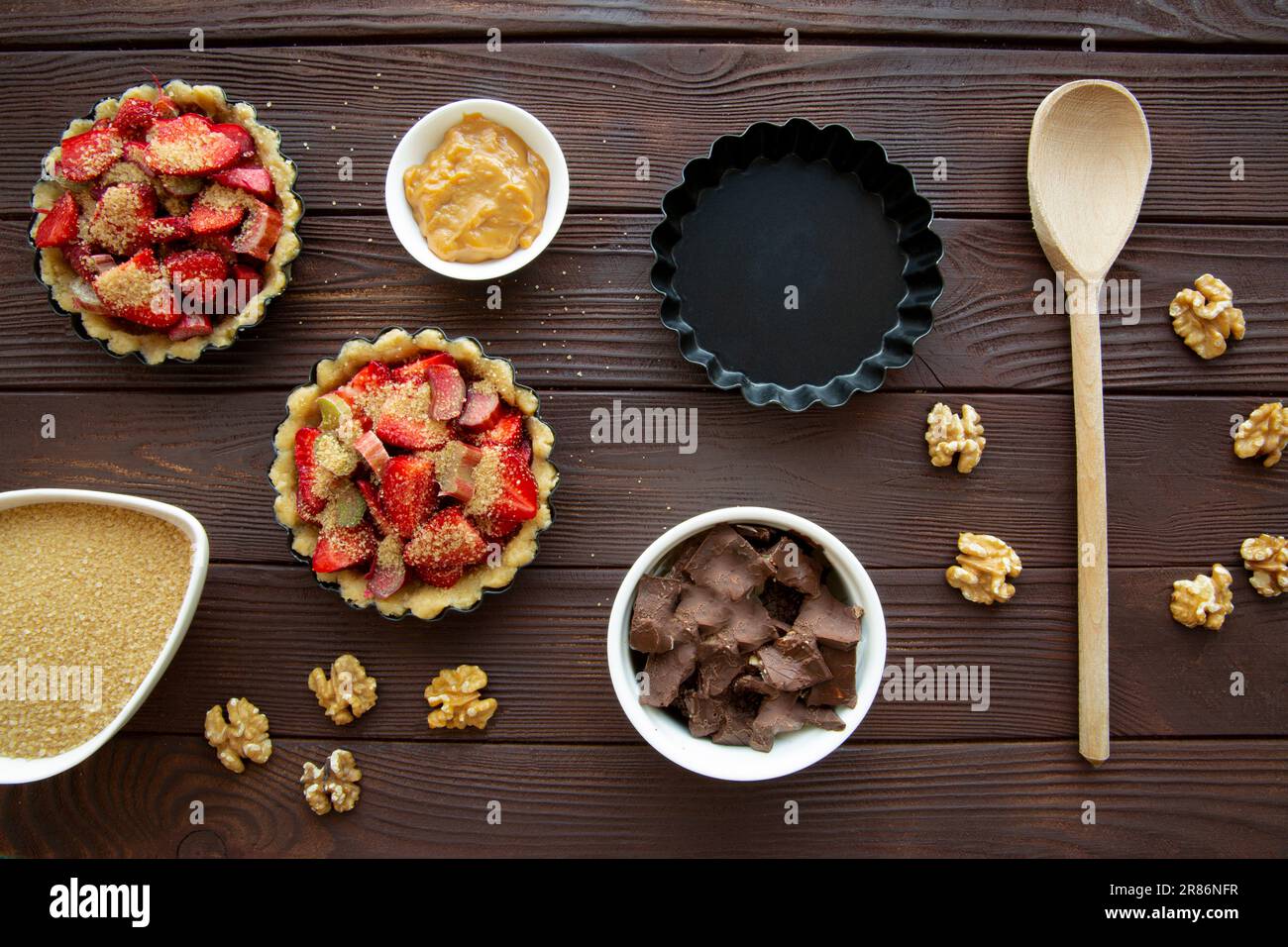 Mini-Törtchen mit Erdbeeren-, Schokoladen- und Nusszubereitung auf braunem Holztisch, Draufsicht. Stockfoto