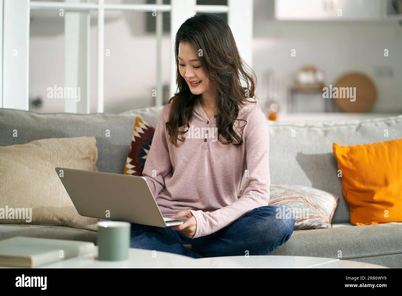 Junge asiatische Geschäftsfrau, die zu Hause auf der Couch sitzt und mit einem Laptop arbeitet Stockfoto