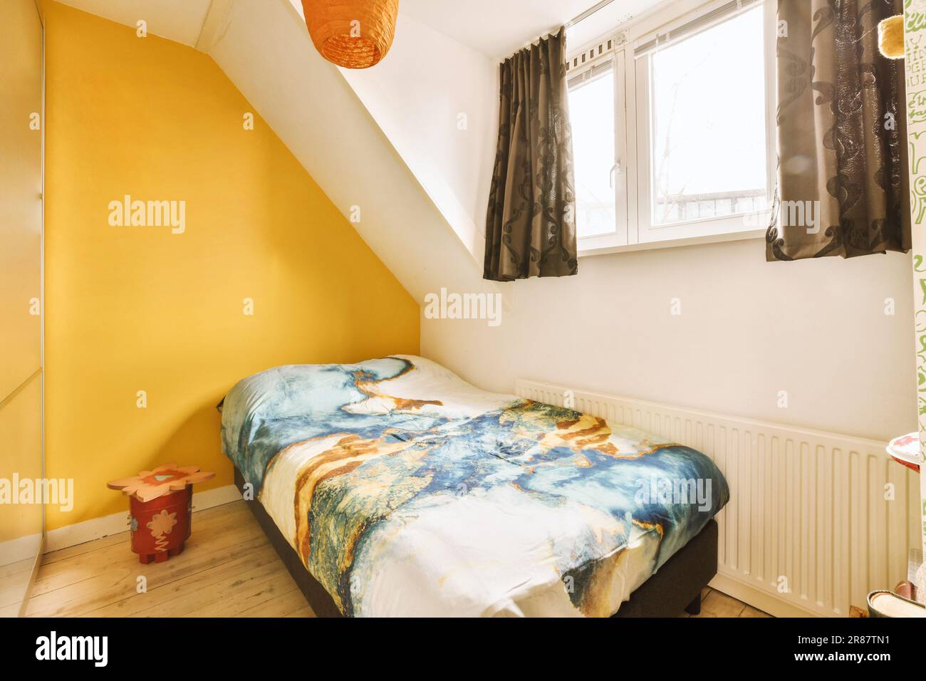 Neben dem Bett befindet sich ein Bett in der Ecke eines Zimmers mit gelben Wänden und weißen Verzierungen am Fenster Stockfoto