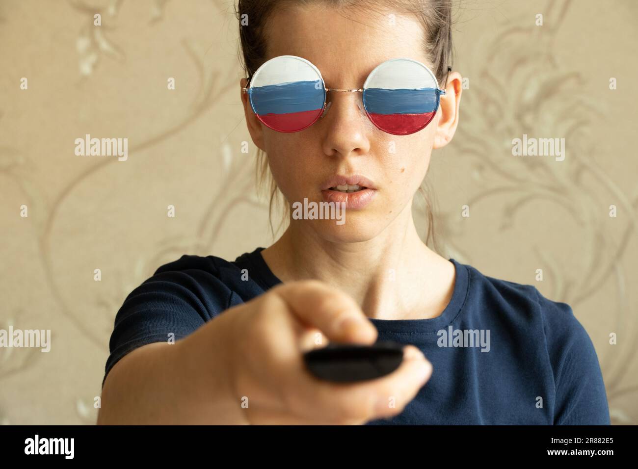 Die russische Flagge auf den Gläsern des Mädchens und in den Händen der Fernbedienung aus dem Fernsehen, Russland und Propaganda aus dem Fernsehen, Lügen und Täuschung Stockfoto