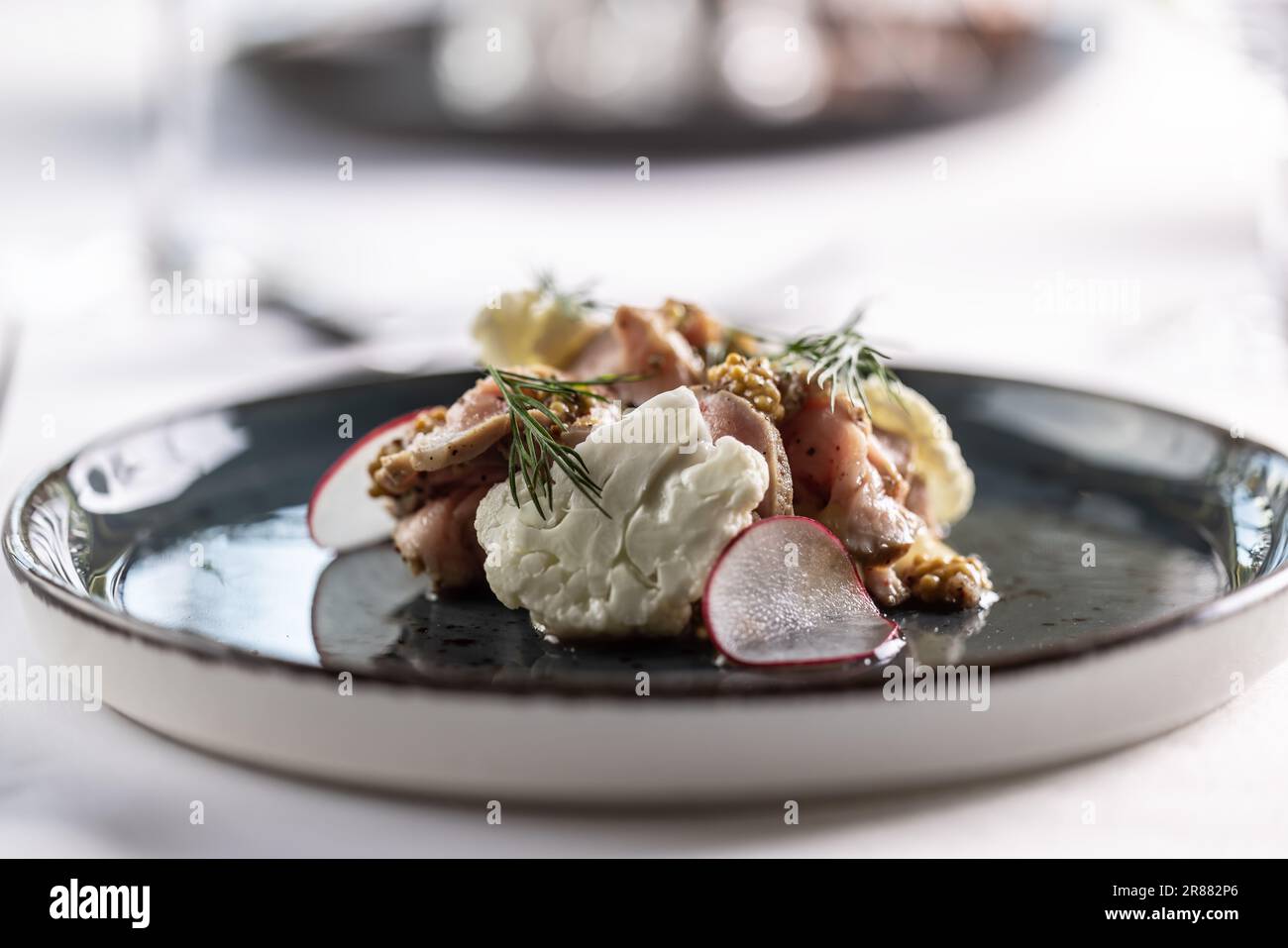Stylen von Speisen mit Schweinefleisch, Blumenkohl, Senfkörnern und Dressing auf einem dunklen Teller. Stockfoto