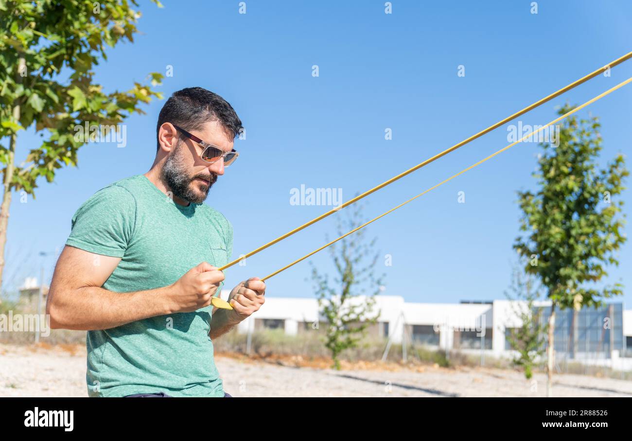 Bärtiger Mann mit Sonnenbrille im Profil beim Bizeps-Training mit einem elastischen Fitnessband in einem Outdoor-Fitnessstudio Stockfoto