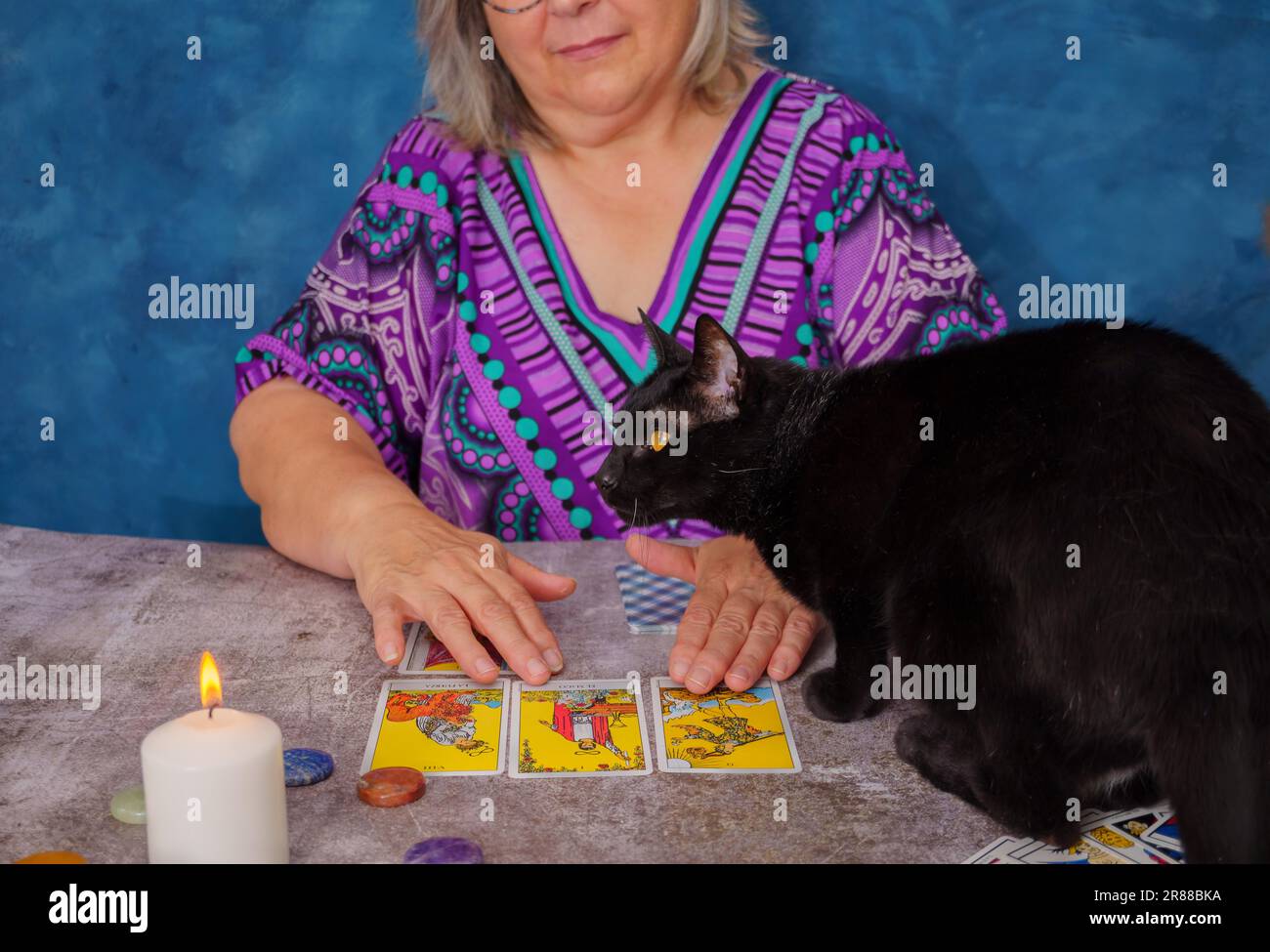Wahrsager liest Tarotkarten mit einer schwarzen Katze auf dem Tisch auf dem Tisch weiße Kerzen Stockfoto