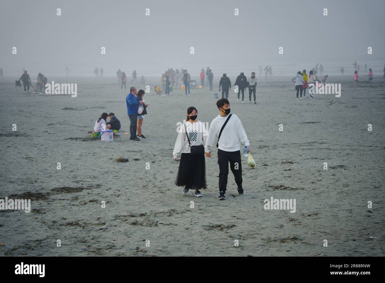 Ein liebevolles Paar, das an einem nebligen Tag am Strand entlang spaziert Stockfoto