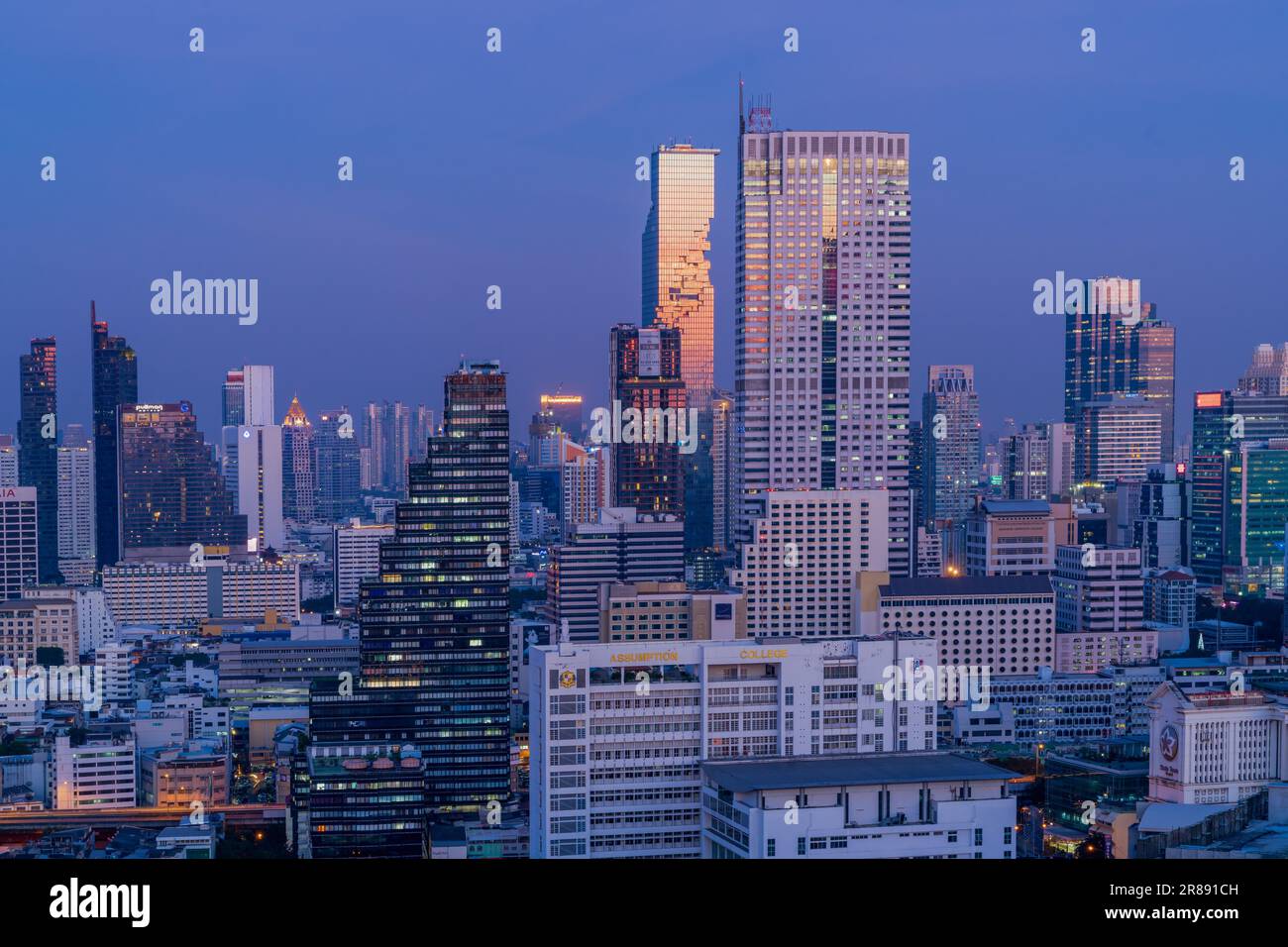 Bangkoks höchstes Gebäude, der Mahanakorn Tower oder das „Tetris Building“, leuchtet orange vor einem violett-blauen Sonnenuntergang Stockfoto