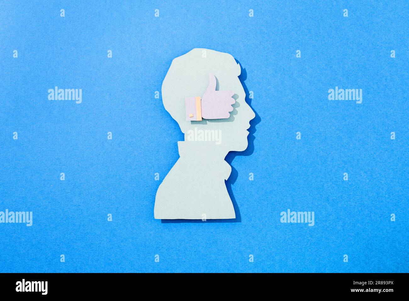 Ein Papierausschnitt aus dem Kopf eines Mannes mit einem ähnlichen Symbol auf blauem Hintergrund Stockfoto