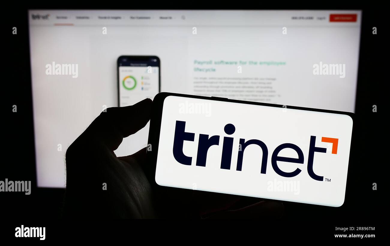 Person, die ein Mobiltelefon mit dem Logo des US-Outsourcing-Unternehmens TriNet Group Inc. Auf dem Bildschirm vor der Unternehmenswebseite hält. Konzentrieren Sie sich auf das Display des Telefons. Stockfoto Person, die ein Mobiltelefon mit dem Logo des US-Outsourcing-Unternehmens TriNet Group Inc. Auf dem Bildschirm vor der Unternehmenswebseite hält. Konzentrieren Sie sich auf das Display des Telefons. Stockfoto
