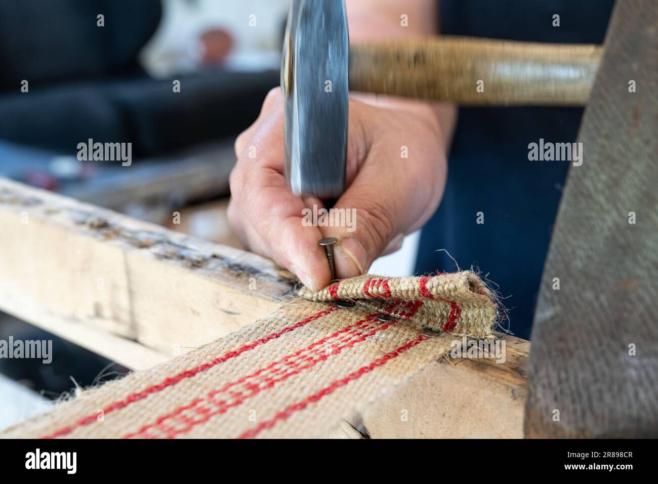 Polster fixiert einen neuen Riemen mit Hammer und Nägeln, um einen alten  Stuhl in seiner Werkstatt zu restaurieren, traditionelle Handwerkskunst,  Kopierraum, Bewegungsunschärfe, Select Stockfotografie - Alamy