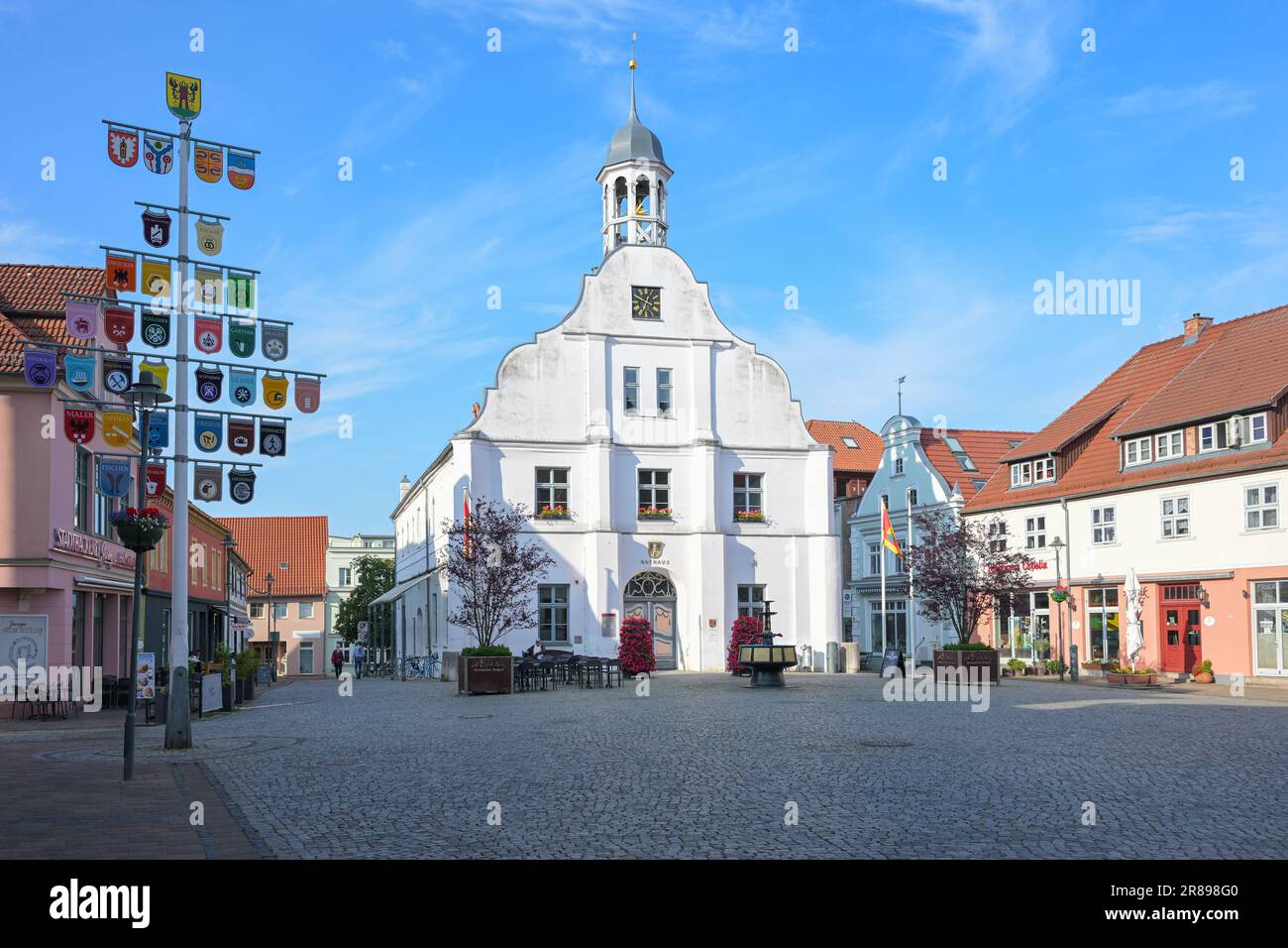 Wolgast, Deutschland, 14. Juni 2023: Rathaus auf dem Marktplatz, Häuser und Mast mit Handwerkssymbolen unter blauem Himmel, historische Altstadt an der Ostsee Stockfoto
