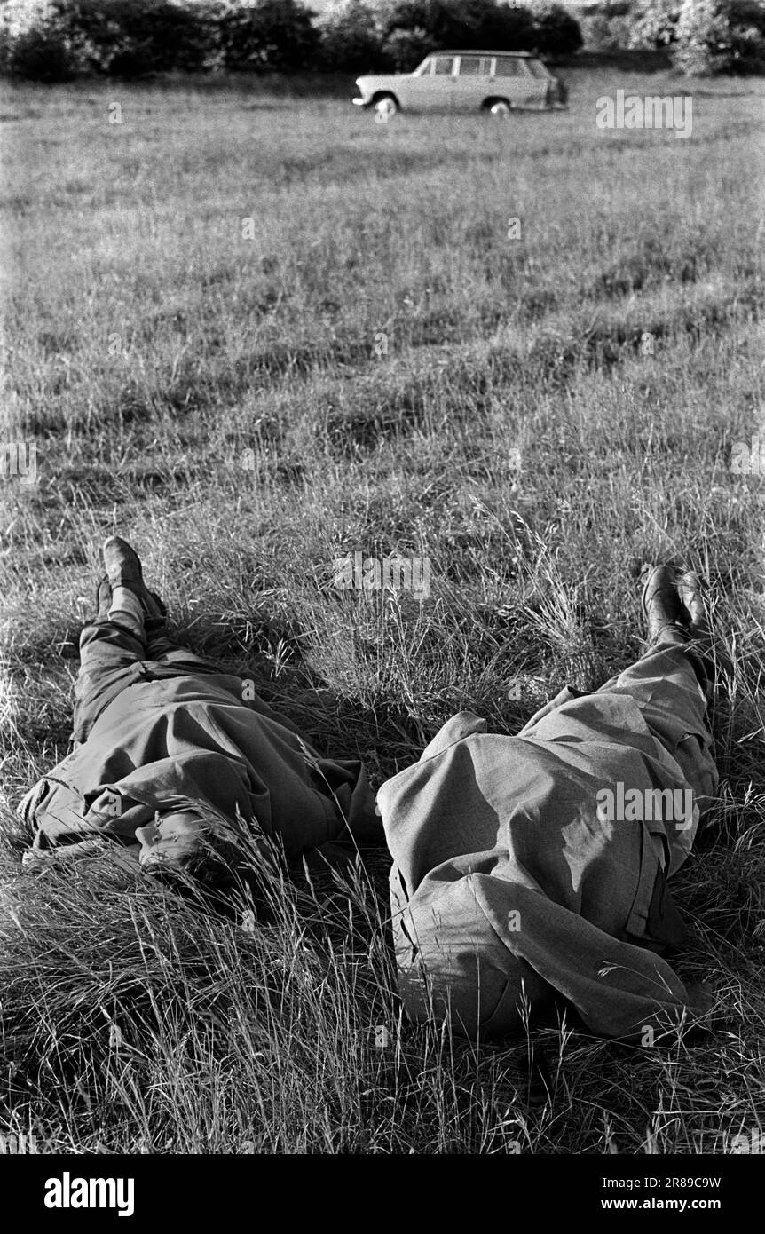 Betrunken ausschlafen, einen Kater. Ein Tag bei den Rennen, zwei Männer bedecken ihre Gesichter in ihren Mänteln, sie schlafen am Ende des Derby, einem jährlichen Pferderennveranstaltungsfestival. Epsom Downs, Surrey, England, ca. 1970 1970er. Juni, Großbritannien. Stockfoto