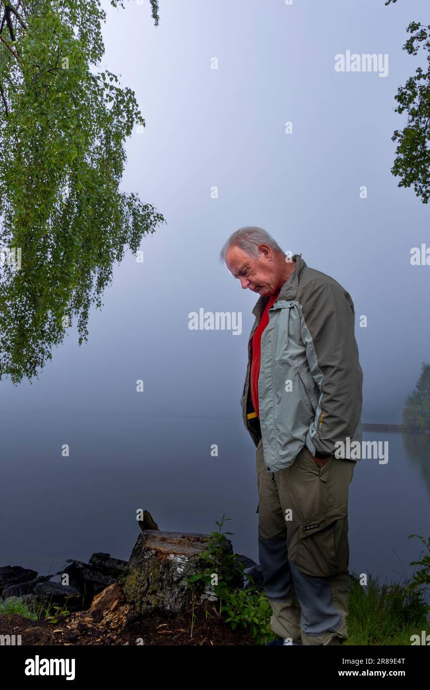 Älterer Mann mit lässiger Kleidung, der auf den Nebel am See schaut Stockfoto