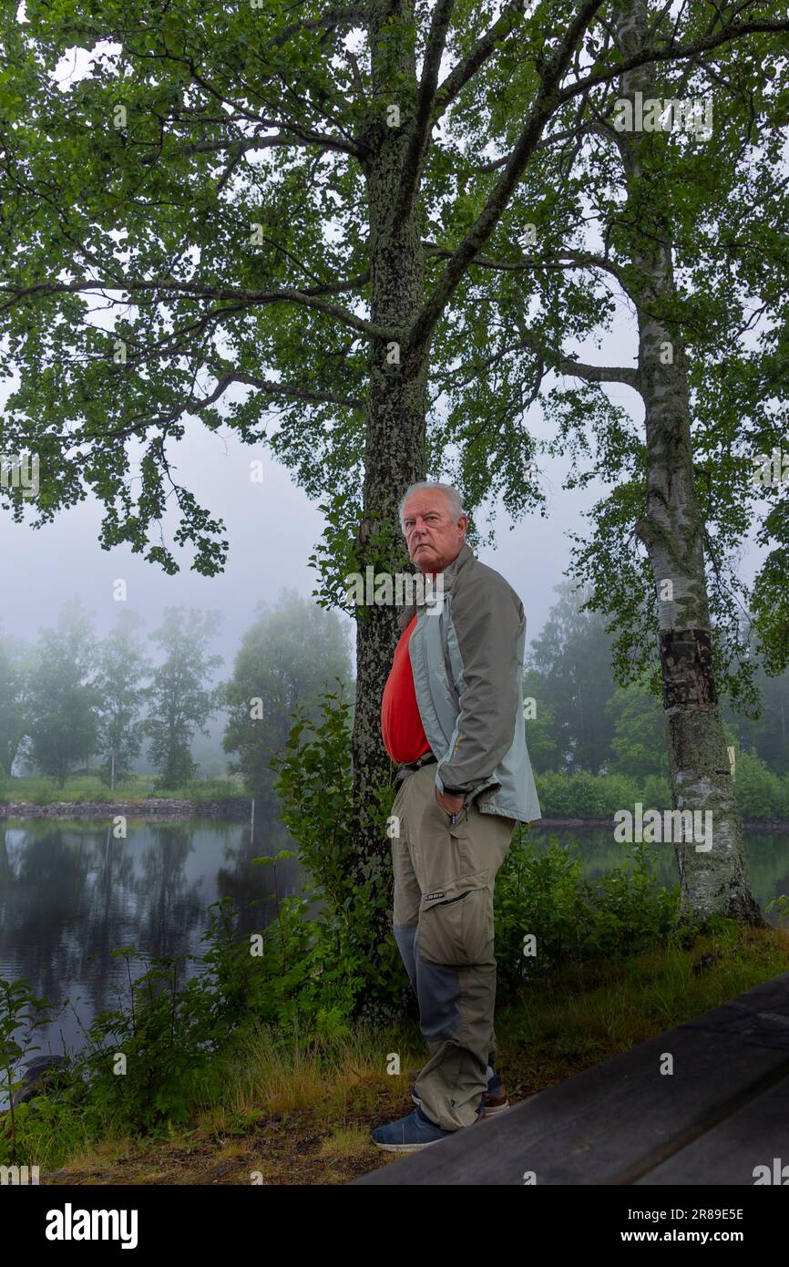 Älterer Mann mit lässiger Kleidung, der auf den Nebel am See schaut Stockfoto