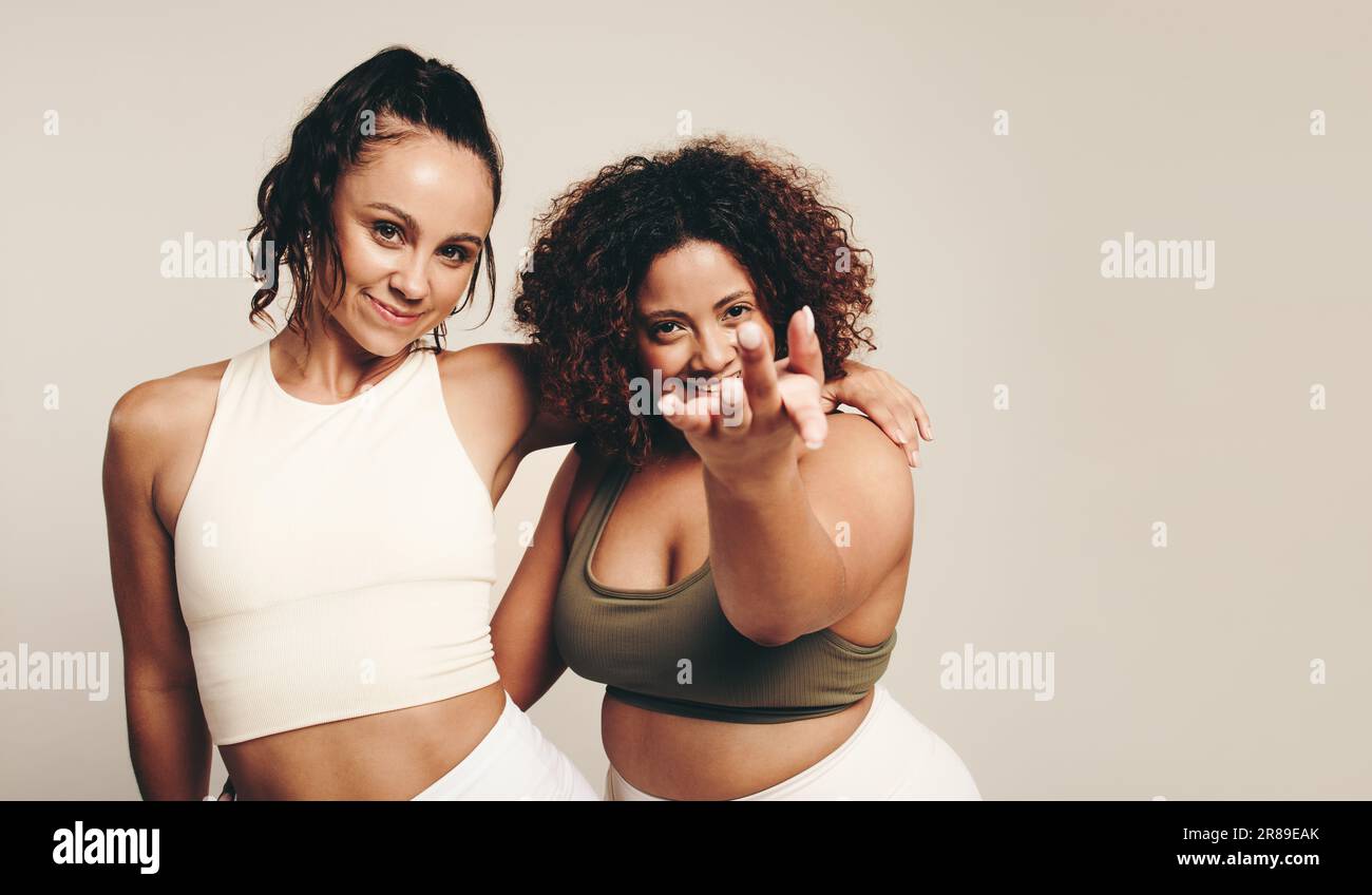Zwei junge Frauen in Sportbekleidung führen mit Energie und Vitalität einen erlebnisreichen Tanz und eine sportliche Übung in einem Studio durch. Fröhliche Sportlerinnen feiern Stockfoto
